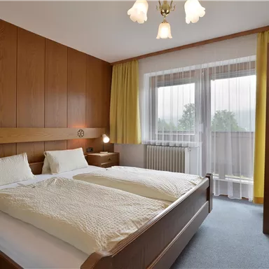 Ein gemütliches Schlafzimmer mit einem Doppelbett und zwei Nachttischen. Große Fenster sorgen für viel Tageslicht.