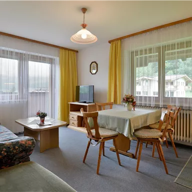 Ein gemütlicher Wohnraum mit einem Sofa, einem Esstisch und Stühlen. Große Fenster sorgen für viel Tageslicht und eine freundliche Atmosphäre.