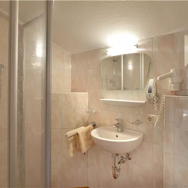 Ein modernes Badezimmer mit einer Dusche und einem Waschbecken. Die Wände sind mit hellen Fliesen dekoriert.