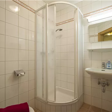 A small bathroom with a shower cabin, a sink, and white tiles. Red towels are added as an accent.