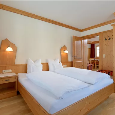 A cozy room with two wooden single beds. The decor is bright and friendly with simple wooden furniture and a warm atmosphere.