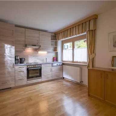 A modern kitchen with wooden cabinets and light walls. The kitchen equipment includes a stove, a refrigerator, and a window with curtains.