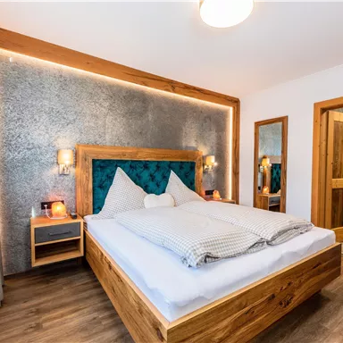 Ein gemütliches Schlafzimmer mit einem Holzbett und eleganter Bettwäsche. Die Wände sind modern gestaltet und es gibt einen schönen Spiegel sowie einen Zugang zum Bad.