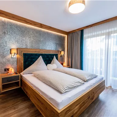 Ein modernes Schlafzimmer mit einem Holzrahmenbett und zwei großen Kissen. Das Fenster lässt viel Tageslicht herein und bietet einen Blick nach draußen.