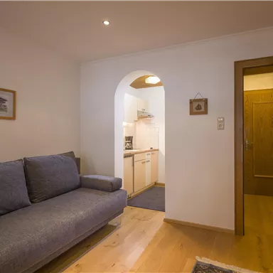 A cozy living room with a gray sofa and a wooden entrance to a kitchen. The room design is modern and inviting.