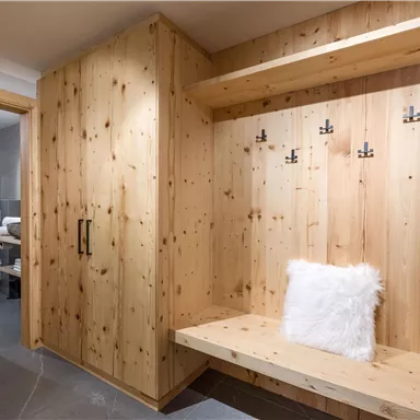 A cozy entrance area with wooden paneling and a bench. Several hooks for jackets and coats are hanging on the wall.