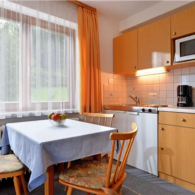Eine gemütliche Küche mit einem Tisch und Stühlen. Die Ausstattung umfasst einen Kühlschrank, eine Mikrowelle und einen Wasserkocher.
