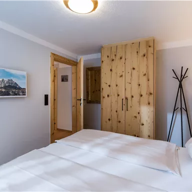 A cozy bedroom with a large bed and wooden shelves. In the background, there is a picture of mountains and a stylish floor lamp.
