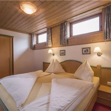 A cozy bedroom with two beds and a wooden ceiling. There are windows with curtains and a wardrobe in the room.