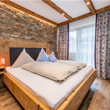 Ein gemütliches Schlafzimmer mit einem Doppelbett und steinernen Wänden. Große Fenster bieten viel Tageslicht und eine TV-Leinwand ist ebenfalls vorhanden.
