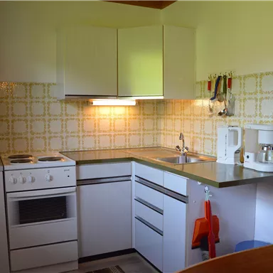 A small, modern kitchen with white furniture and a stylish tile design. It is equipped with a stove, a sink, and various kitchen appliances.