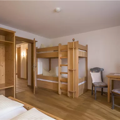 Ein gemütliches Schlafzimmer mit einem Etagenbett und einem Tisch. Die Wände sind hell, und es gibt holzene Möbel, die eine warme Atmosphäre schaffen.