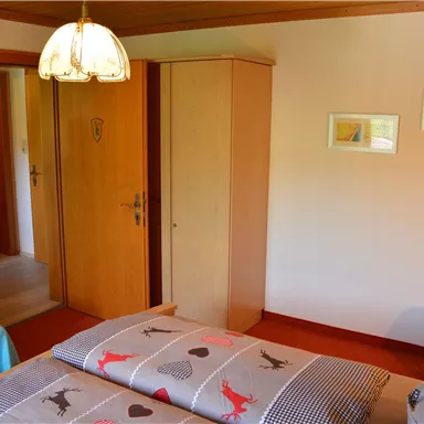 A cozy bedroom with a double bed, a wardrobe, and a wooden ceiling. There is also an armchair and some pictures on the wall.