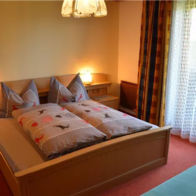 A cozy bedroom with a large bed and two pillows. The room has a window with curtains and soft lighting.
