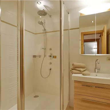 Ein modernes Badezimmer mit einer Dusche, einem Waschbecken und Holzschränken. Es gibt zusätzliche Handtücher und einen Fön für den Komfort.