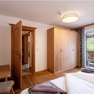 Ein helles Schlafzimmer mit Holzmöbeln und einem großen Fenster. Es gibt ein Bett, einen Schreibtisch und einen Zugang zu einem Balkon.