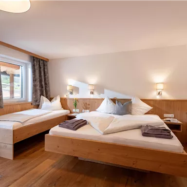 Ein gemütliches Schlafzimmer mit einem Doppelbett und einem Einzelbett. Die Wände sind hell, und es gibt warme Holzdetails sowie sanfte Beleuchtung.
