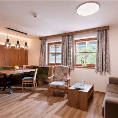 Eine gemütliche Wohnzimmer mit Holzmöbeln, einem Essbereich und großen Fenstern. Ein Sofa und ein Sessel ergänzen den einladenden Raum.