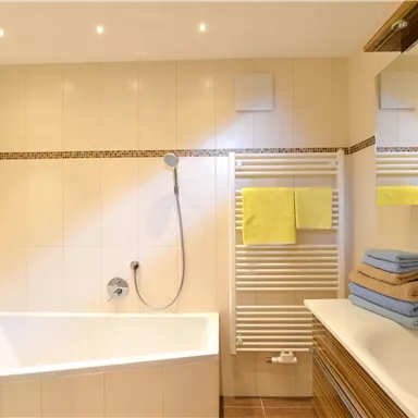 Ein modernes Badezimmer mit einer Badewanne und einer Dusche. Handtücher in verschiedenen Farben liegen ordentlich auf dem Waschbecken.