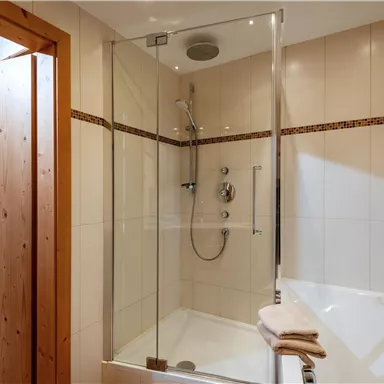 Ein modernes Badezimmer mit einer gläsernen Duschkabine und einer Badewanne. Die Wände sind gefliest und die Tür ist aus Holz.