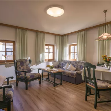 Ein gemütliches Wohnzimmer mit bequemen Möbeln und großen Fenstern. Die Atmosphäre ist freundlich und einladend, mit Blumendekor und sanften Farben.