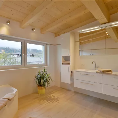 Ein modernes Badezimmer mit Holzdecken und viel natürlichem Licht. Es verfügt über ein Waschbecken mit Schränken und eine Badewanne.