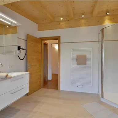 Ein modernes Badezimmer mit Holzdecke und eleganten weißen Möbeln. Es verfügt über eine Dusche und viel Licht.