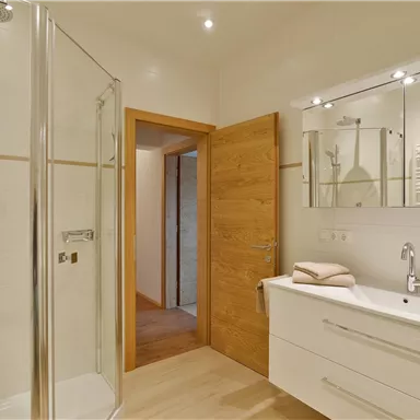 Ein modernes Badezimmer mit einer gläsernen Dusche und einem eleganten Waschbecken. Die Wände sind hell und der Boden ist aus Holz.