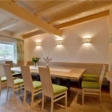 Ein heller Essbereich mit Holzdecke und großen Fenstern. Der Tisch ist mit Stühlen und einem dekorativen Blumenarrangement ausgestattet.