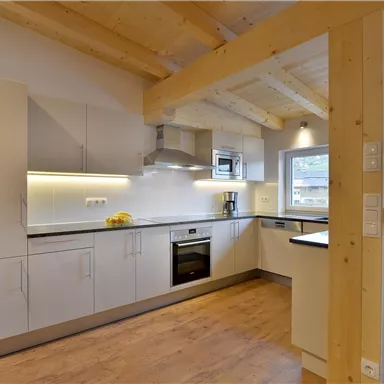 Eine moderne Küche mit Holzdecken und klaren Linien. Die Küchenschränke sind in Weiß gehalten und der Raum ist hell und einladend.