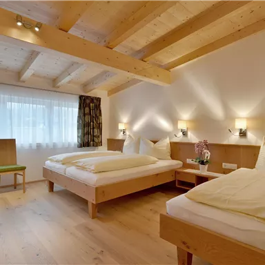 Ein gemütliches Schlafzimmer mit zwei einzelnen Betten und Holzdecke. Der Raum ist hell und schlicht eingerichtet, mit einem Fenster, das viel Licht hereinlässt.