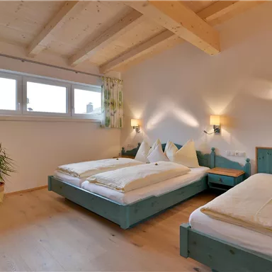 Ein gemütliches Schlafzimmer mit zwei Betten und Holzdecken. Große Fenster sorgen für viel Tageslicht und die Einrichtung ist einfach und einladend.