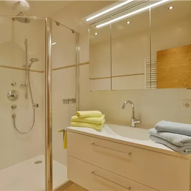 Ein modernes Badezimmer mit einer Glasdusche und einem Waschbecken. Bunte Handtücher liegen ordentlich auf der Halterung.