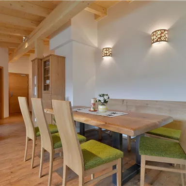 Ein gemütlicher Essbereich mit einem Holz-Tisch und Stühlen in sanften Farben. An den Wänden sind stilvolle Lampen angebracht, und ein Fernseher steht in der Ecke.
