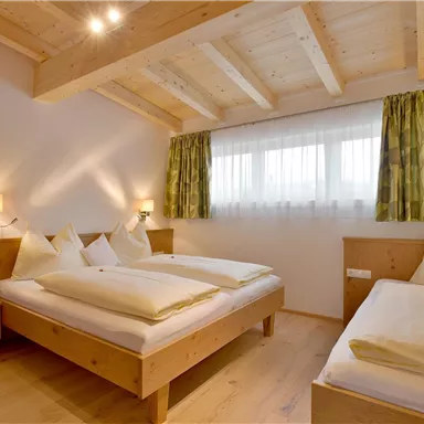 Ein gemütliches Schlafzimmer mit zwei Betten und Holzdetails. Helle Vorhänge und sanftes Licht schaffen eine einladende Atmosphäre.