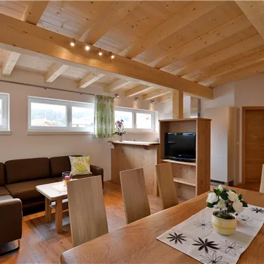Ein modernes Wohnzimmer mit Holzdecken und großen Fenstern. Es gibt ein Sofa, einen Tisch und eine kleine Schüssel mit Blumen auf dem Tisch.