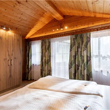 Ein gemütliches Schlafzimmer mit Holzbalkendecke und großen Fenstern. Die Wände sind mit elegantem Dekor und einem modernen Kleiderschrank gestaltet.