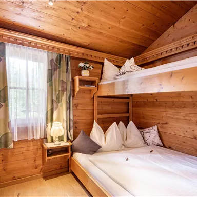 Ein gemütliches Zimmer mit Holzvertäfelung und zwei Betten. Die Fenster lassen viel Licht herein und die Dekoration ist schlicht und einladend.