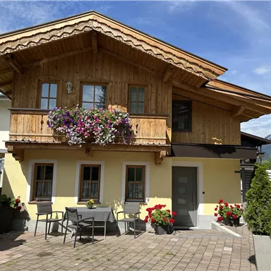 Ein schönes Holzhaus mit einem Balkon, der mit Blumen geschmückt ist. Der Innenhof ist mit Tischen und Pflanzen ausgestattet, ideal zum Entspannen.