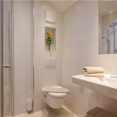 Ein modernes Badezimmer mit einer Dusche, einem Waschbecken und einer Toilette. Es hat eine helle, freundliche Atmosphäre mit einem kleinen Blumendekor.