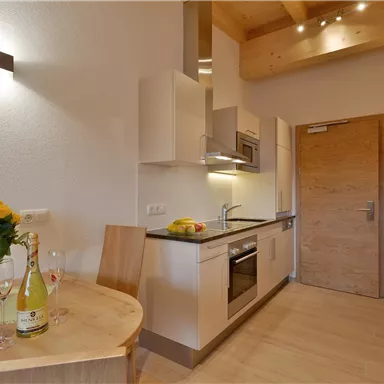 Moderne Küche mit hellen Möbeln und Holzdecken. Ein Tisch mit Blumen und Getränken lädt zum Verweilen ein.