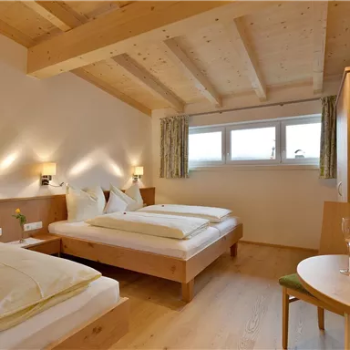 Ein stilvolles Zimmer mit zwei Betten und Holzdecken. Es gibt einen kleinen Tisch mit Blumen und eine gemütliche Atmosphäre.
