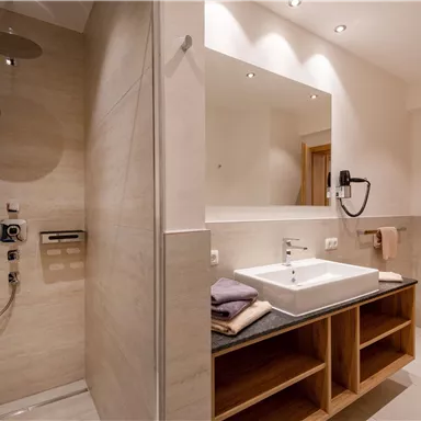 Ein modernes Badezimmer mit einer Dusche, einem Waschbecken und Holzregalen. Die Wände sind hell und die Beleuchtung ist angenehm.