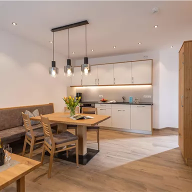 Ein modernes Wohnzimmer mit einer gemütlichen Sitzecke und einem Essbereich. Die Küche ist gut ausgestattet und die Beleuchtung schafft eine einladende Atmosphäre.