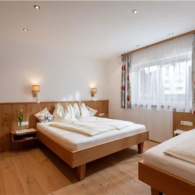 Ein gemütliches Schlafzimmer mit zwei Einzelbetten und warmem Holzinterieur. Das Zimmer hat große Fenster mit viel Tageslicht und moderne Beleuchtung.