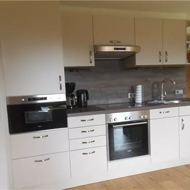 A modern kitchen with bright cabinets and a stainless steel sink. The equipment includes an oven, a microwave, and coffee machines.