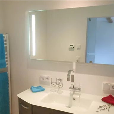 A modern bathroom with a sink and a mirror. Towels in blue and red hang on a towel rack.