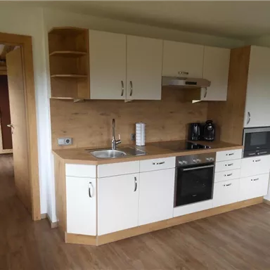 A modern kitchen with wooden accents and white cabinets. It is equipped with a stove, a refrigerator, and a sink.