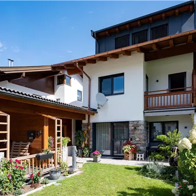 A modern house with a beautiful garden and flowers. The sky is clear and blue, creating an inviting atmosphere.
