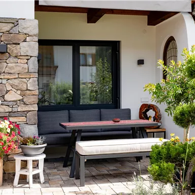 A cozy terrace with a wooden bench and a table. Flowers and plants decorate the entrance area.